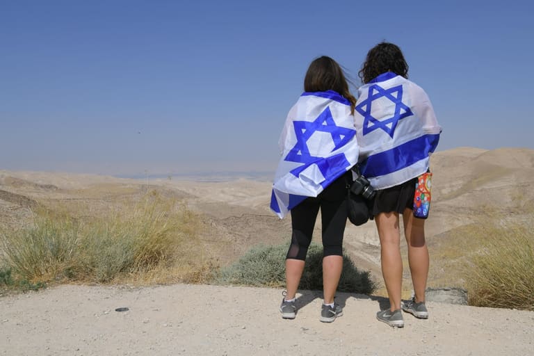 Two women wrapped in Israeli flags looking out over the desert