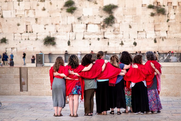 Women in red shawls standing arm in arm facing the Western Wall