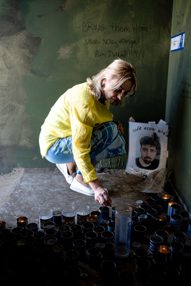 A woman lighting a memorial candle beside a wall of messages