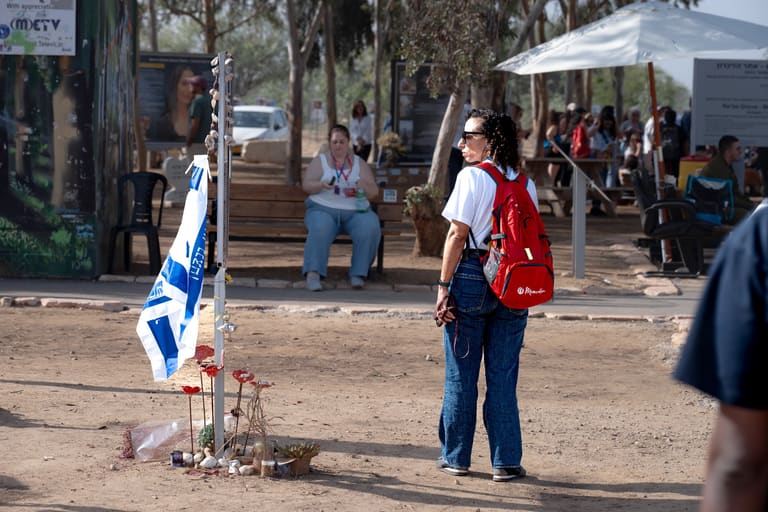 A woman standing quietly at a memorial marker in the Re'im grove