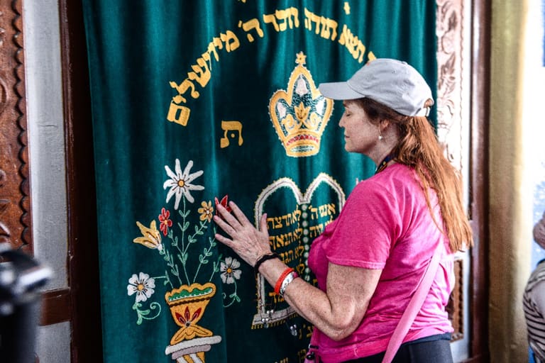 A woman resting her hands on an embroidered Torah ark curtain