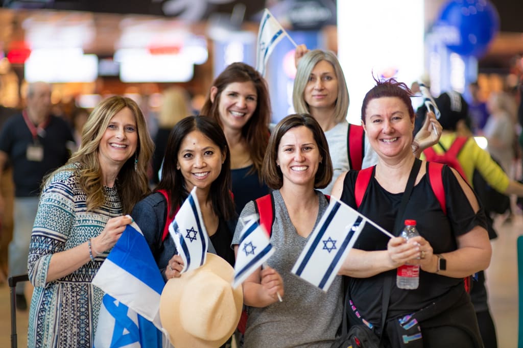 Momentum sisters smiling together at the airport, holding Israeli flags